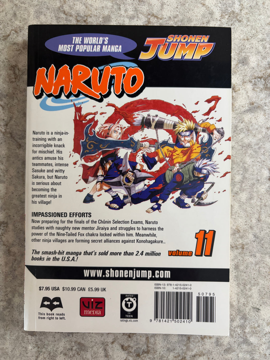 Back cover of Naruto Volume 11 manga book published by Shonen Jump, featuring colorful anime artwork of Naruto, Sasuke, and Sakura, with pricing and barcode details at the bottom, photographed on a gray textured surface.